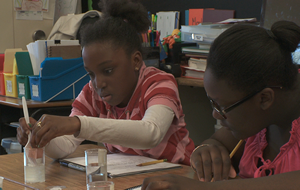 Photograph of two girls measuring the volume of a cube using water displacement.