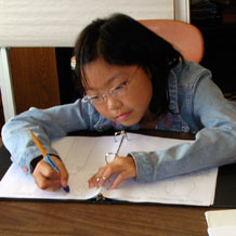 Girl taking notes in a notebook and materials on table.